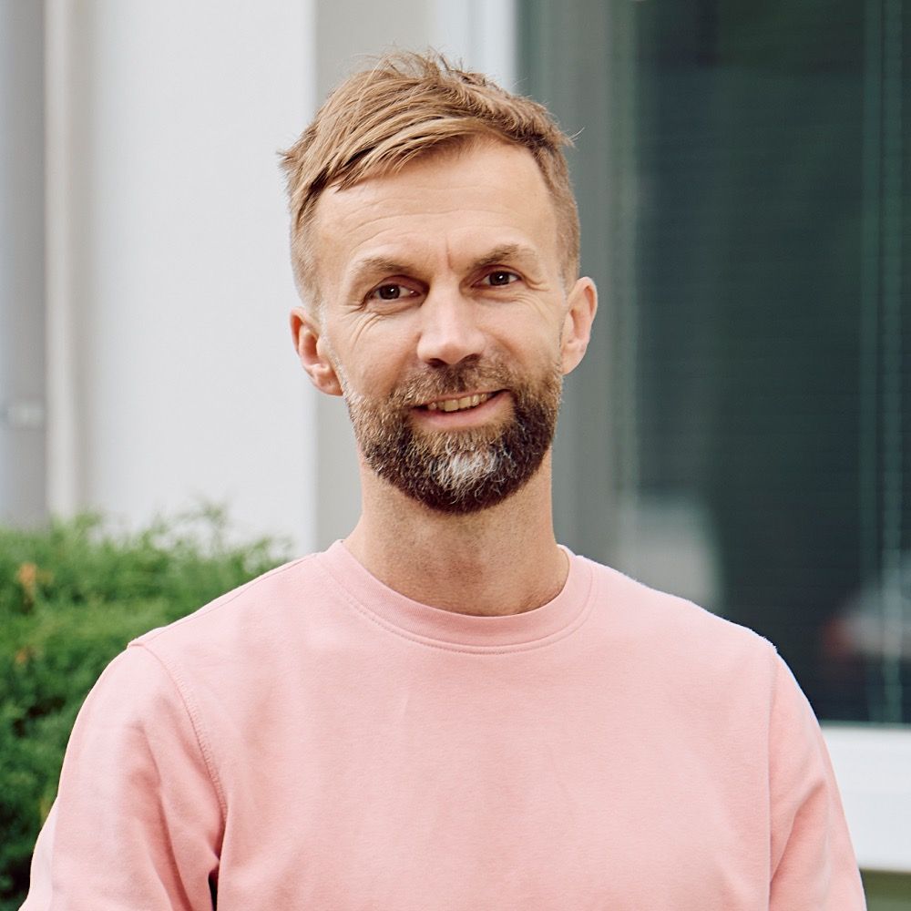 Portrait von Marcel Rau, Ansprechpartner und IT-Experte bei DigiQon, im rosa Pullover vor dem Bürogebäude.