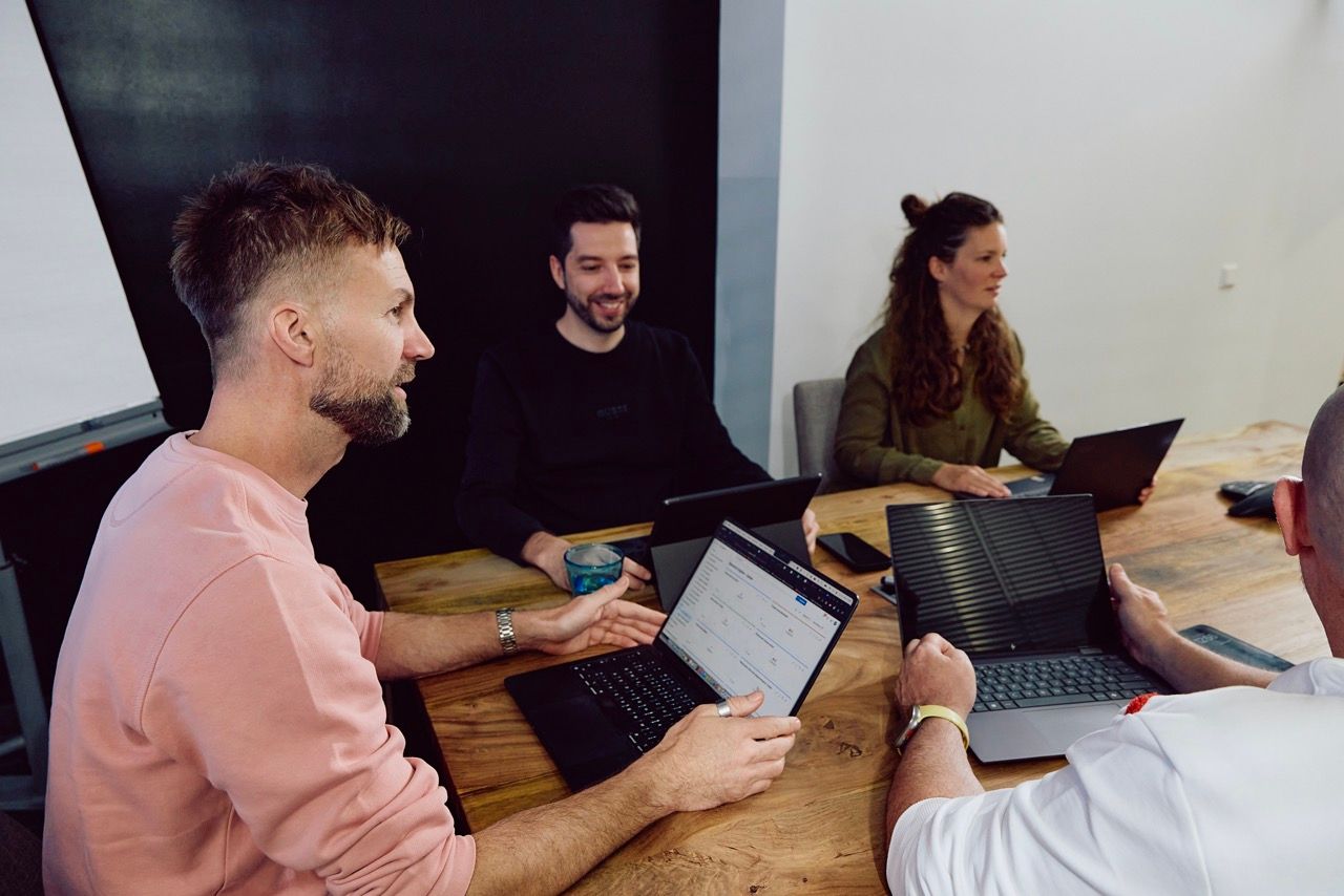 Vier DigiQon-Mitarbeitende sitzen mit Laptops um einen großen Holztisch im Besprechungsraum und arbeiten gemeinsam an einem IT-Projekt.
