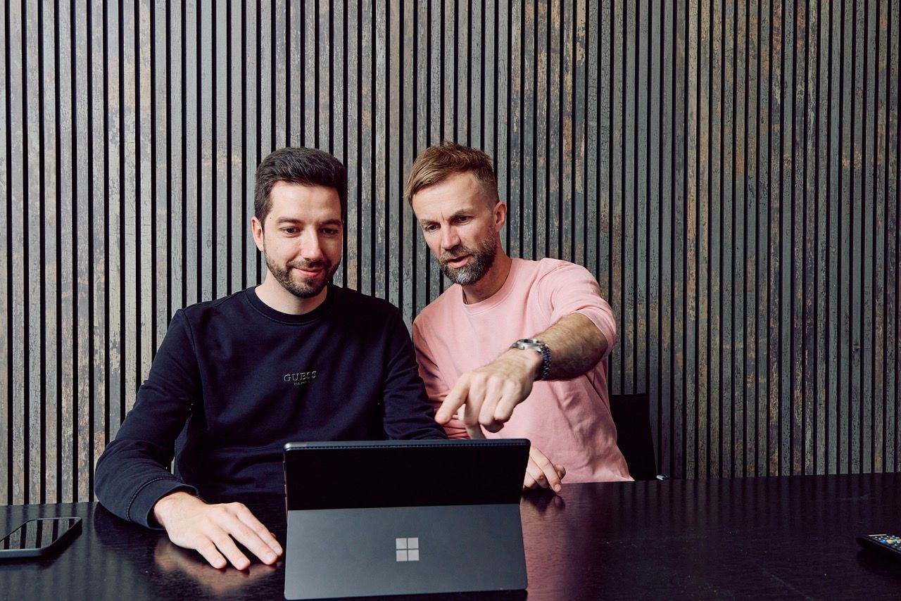 Zwei Männer blicken gemeinsam auf ein Surface-Tablet, einer zeigt auf den Bildschirm.