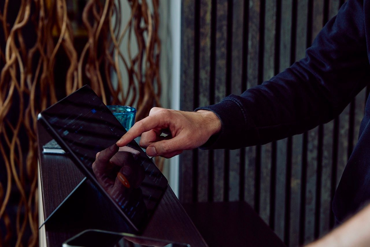Hand bedient den Touchscreen eines Tablets in einem abgedunkelten Empfangsbereich.